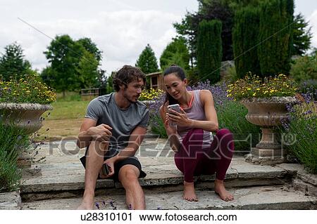 Man and woman practicing yoga in garden, looking at smartphones on patio View Large Photo Image Stock Image - Man and woman practicing yoga in garden, looking at smartphones on patio. Fotosearch