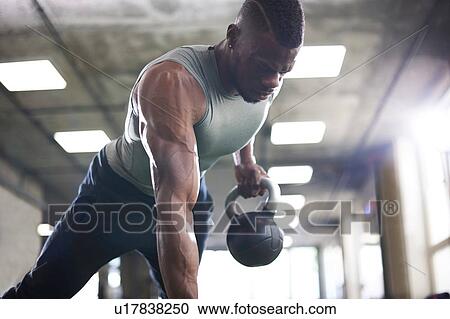 Stock Image - Man doing plank with kettlebells in gym. Fotosearch