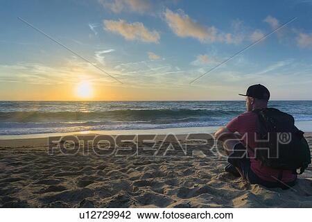 Stock Image - Man enjoying sunset on beach. Fotosearch