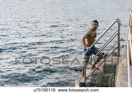 Stock Photograph - Man going up steps from sea. Fotosearch