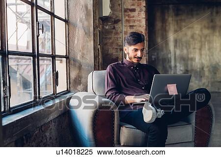 Stock Photography - Man in armchair using laptop. Fotosearch