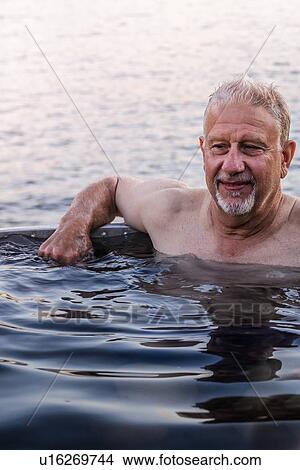 Picture - Man in hot tub by lakeside, Johnstone Strait, Telegraph Cove, Canada. Fotosearch
