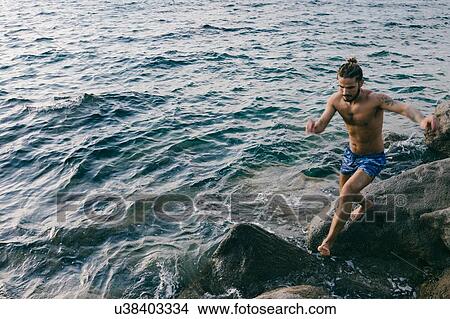 Picture - Man jumping from rock to rock in sea. Fotosearch