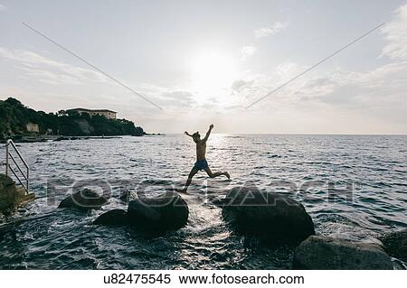 Stock Photography - Man jumping from rock to rock in sea. Fotosearch