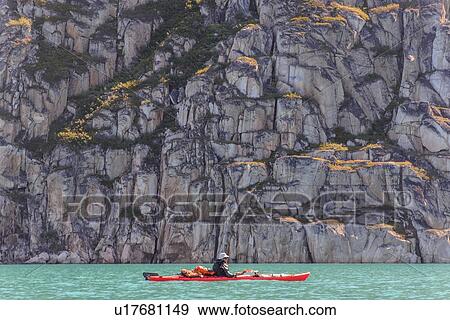 Stock Photo - Man kayaking near cliff, Narsaq, Vestgronland, Greenland. Fotosearch
