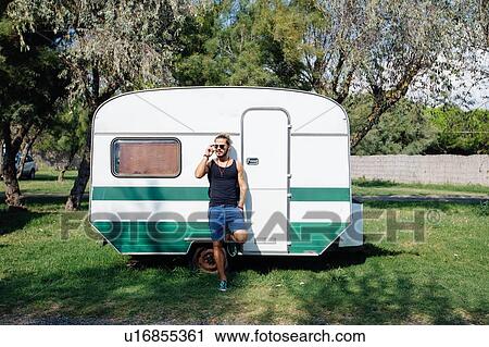Stock Image - Man leaning against caravan. Fotosearch