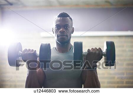 Stock Image - Man lifting dumbbells in gym. Fotosearch