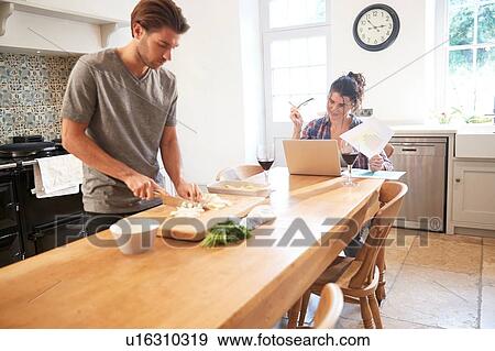 Man preparing vegetables at kitchen table, girlfriend using laptop View Large Photo Image Stock Photo - Man preparing vegetables at kitchen table, girlfriend using laptop. Fotosearch