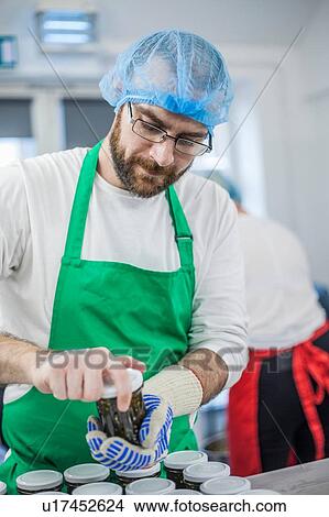 Picture - Man putting lids on jars of jam in industrial kitchen. Fotosearch
