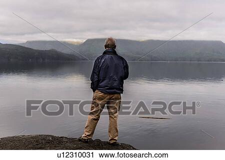 Stock Image - Man relaxing by lakeside, Johnstone Strait, Telegraph Cove, Canada. Fotosearch
