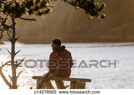 Stock Image - Man relaxing by lakeside, Johnstone Strait, Telegraph Cove, Canada. Fotosearch