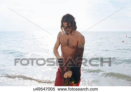 Stock Photography - Man removing clothes by sea. Fotosearch