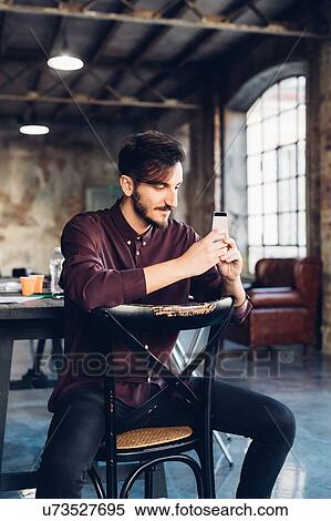 Man sitting back to front on chair using smartphone View Large Photo Image Stock Photography - Man sitting back to front on chair using smartphone. Fotosearch