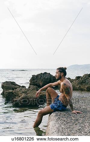 Stock Photograph - Man sitting on edge of sea. Fotosearch
