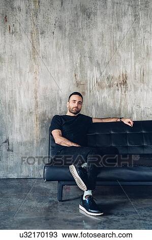 Man sitting on sofa, concrete wall in background View Large Photo Image Stock Image - Man sitting on sofa, concrete wall in background. Fotosearch
