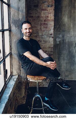 Stock Image - Man sitting on swivel stool by window. Fotosearch