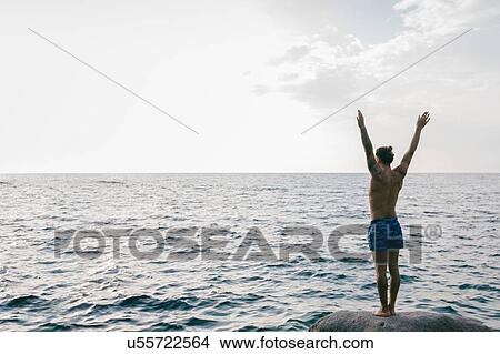 Man standing on rock in sea View Large Photo Image Picture - Man standing on rock in sea. Fotosearch