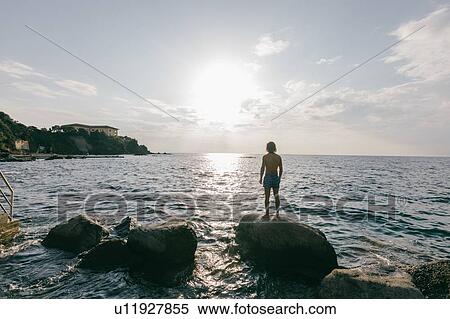 Man standing on rock in sea View Large Photo Image Stock Photography - Man standing on rock in sea. Fotosearch