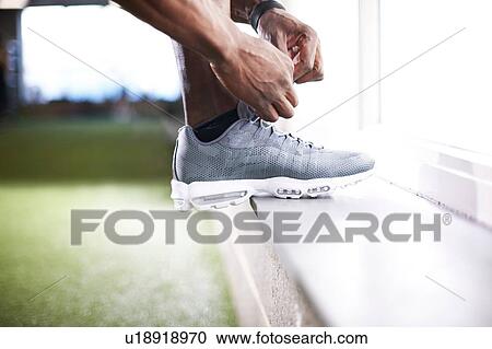 Stock Image - Man tying shoelace in gym. Fotosearch
