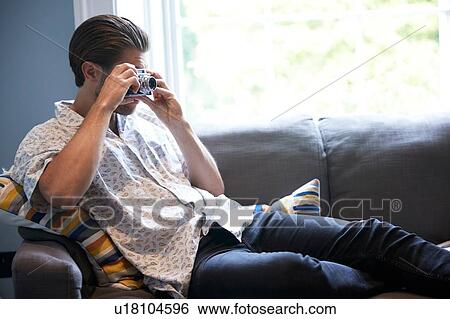 Stock Photograph - Man using camera on sofa. Fotosearch