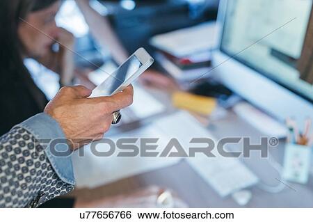 Stock Photograph - Man using cellphone at desk. Fotosearch
