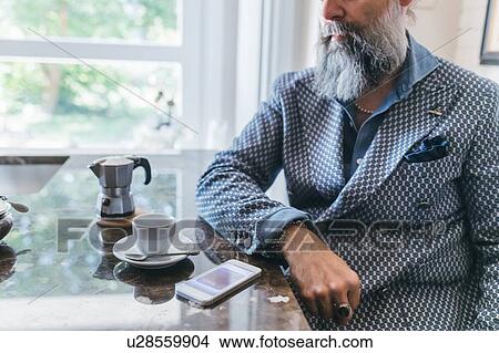 Picture - Man using cellphone over coffee in kitchen. Fotosearch