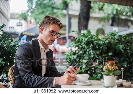 Stock Image - Man using cellphone while having morning coffee at outdoor cafe, Budapest, Hungary. Fotosearch
