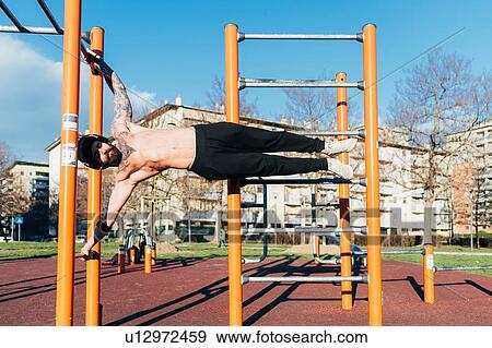 Stock Photo - Man using horizontal ladder in outdoor gym. Fotosearch