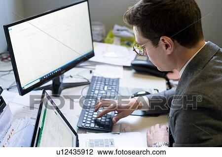 Man using laptop and desktop in office View Large Photo Image Stock Image - Man using laptop and desktop in office. Fotosearch