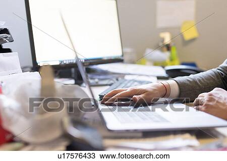 Stock Image - Man using laptop and desktop in office. Fotosearch