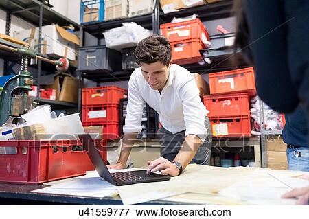 Stock Photo - Man using laptop in demonstration in warehouse. Fotosearch