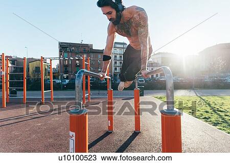 Stock Image - Man using parallel bars in outdoor gym. Fotosearch
