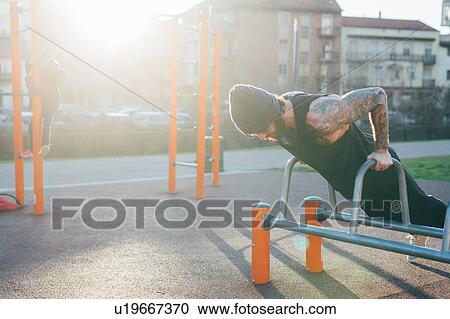 Stock Image - Man using push up bar in outdoor gym. Fotosearch