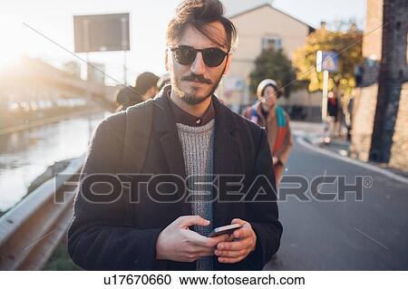 Stock Image - Man walking by canal, friends in background, Milan, Italy. Fotosearch