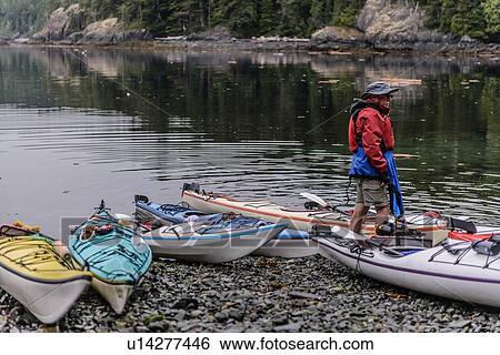 Stock Photograph - Man with sea kayaks on lakeside, Johnstone Strait, Telegraph Cove, Canada. Fotosearch