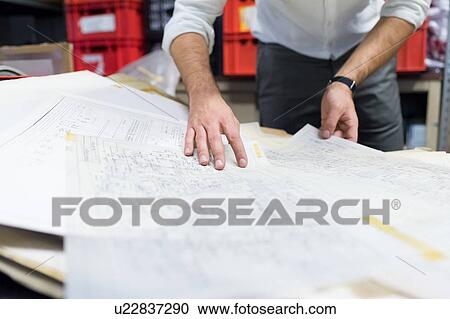 Stock Image - Man working on charts and plans in warehouse. Fotosearch