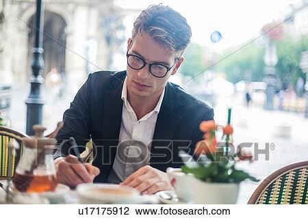 Stock Image - Man writing while having morning coffee at outdoor cafe, Budapest, Hungary. Fotosearch