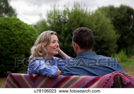 Stock Image - Mature couple sitting on garden bench. Fotosearch