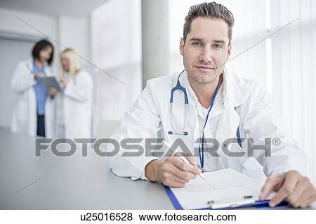 Mature male doctor doing paperwork and looking towards camera. View Large Photo Image Stock Photo - Mature male doctor doing paperwork and looking towards camera.. Fotosearch