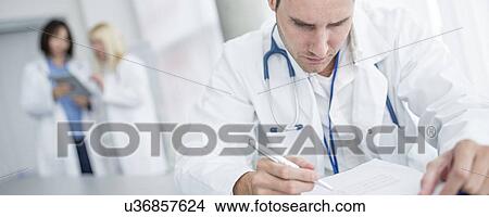 Picture - Mature male doctor doing paperwork, cropped portrait.. Fotosearch