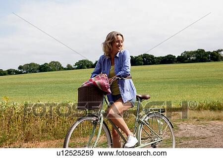 Mature woman looking sideways from bicycle on rural road View Large Photo Image Stock Photo - Mature woman looking sideways from bicycle on rural road. Fotosearch
