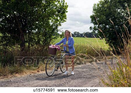 Mature woman pushing bicycle along rural road View Large Photo Image Stock Image - Mature woman pushing bicycle along rural road. Fotosearch