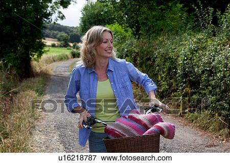 Mature woman pushing bicycle along rural road View Large Photo Image Stock Photo - Mature woman pushing bicycle along rural road. Fotosearch