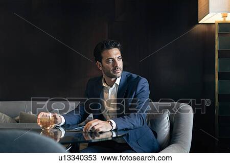 Stock Image - Mid adult businessman sitting in hotel table looking away. Fotosearch