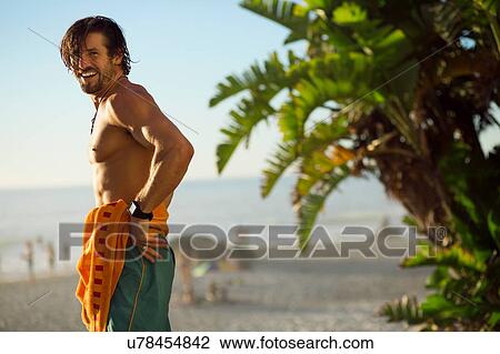 Stock Image - Mid adult male surfer on beach, portrait, Camps Bay Beach, Cape Town, South Africa. Fotosearch