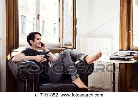 Mid adult man sitting on armchair chatting on smartphone View Large Photo Image Stock Image - Mid adult man sitting on armchair chatting on smartphone. Fotosearch