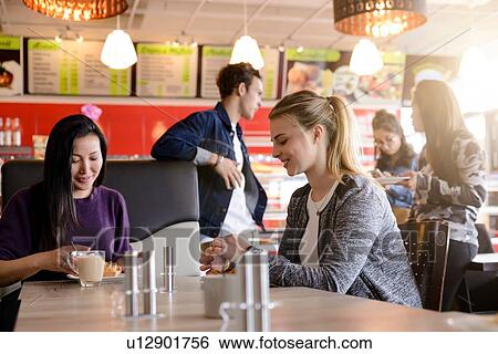 Stock Photograph - Mid adult woman and friend having coffee in cafe. Fotosearch