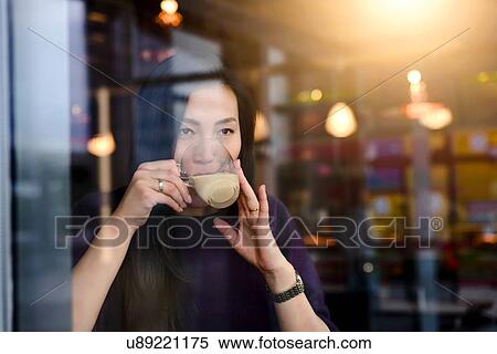 Stock Photography - Mid adult woman drinking coffee in cafe window seat. Fotosearch