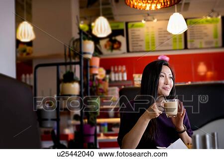 Stock Image - Mid adult woman holding coffee cup in cafe. Fotosearch
