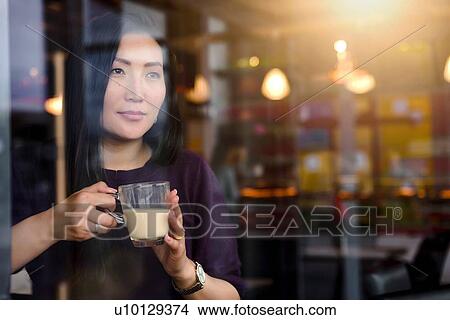 Mid adult woman with coffee looking out from cafe window seat View Large Photo Image Picture - Mid adult woman with coffee looking out from cafe window seat. Fotosearch